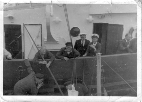 Photo:Left to right:  The white arm is that of Bob Patterson the Tug Engineer.  Hanging over the side is Steve Payne, leaning over the side is Charlie Stone,  next to Charlie is Jim Still, then low down over the side is my Brother George Still,  peaked cap left is Capt. "Paddy" Pringle,  then the Mate  "Jock Still" and just exited the door is Bob Martin the Harbour works manager.